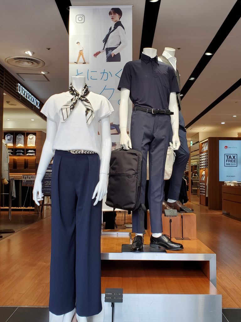 マネキン3体の画像。正面、レディース衣裳。白のTシャツにブラウン系のドット柄スカーフを首元に。ネイビーのワイドパンツを合わせている。
右側奥のマネキンは、メンズのビジネスカジュアルスタイル。ネイビーのポロシャツ。ネイビーのスラックス手にはビジネスリュック。ブラックシューズ。ベルトもブラック。
更に右奥のマネキンは、前に位置しているマネキンと被ってしまって、ほぼこちらからは見えない。メンズの衣裳。白のシャツにカーキのベストネイビーのパンツスタイル。
画像に alt 属性が指定されていません。ファイル名: 666%E2%98%85%E5%BA%97%E5%86%85%E5%86%99%E7%9C%9F%E2%91%A1-768x1024.jpg